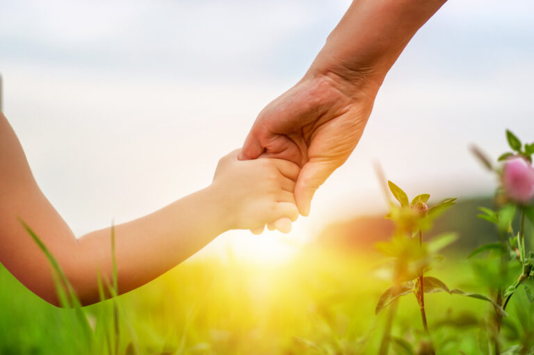 Hands of mother and daughter holding each other on field